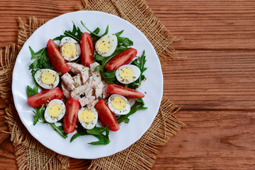 Green vegetable salad, chicken and quail eggs. Salad with tomatoes, arugula, quail eggs, chicken fillet and spices on a plate and a wooden background with copy space. Healthy and tasty food. Top view 