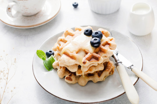 Belgian waffles with cream honey and blueberries on white plate. Bright breakfast image