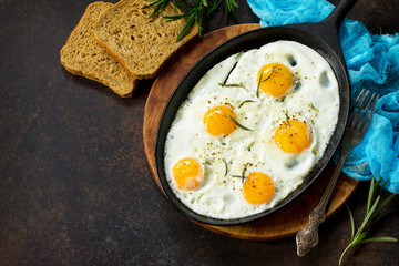 Scrambled eggs on a cast-iron frying pan and an avocado sandwich with fresh sliced avocado and pine nuts on a dark slate or stone background. Top view.