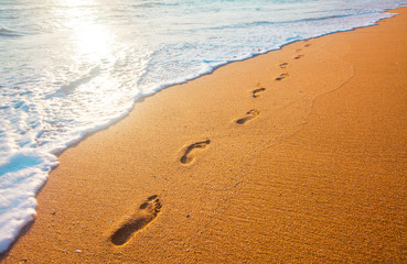 beach, wave and footprints at sunset time