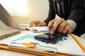 businessman hand working with finances about cost and calculator and laPtop with tablet and smartphone on withe desk in modern office in morning light
