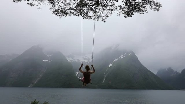 slow motion of beautiful young woman on the swing in fjord Norway, dream concept