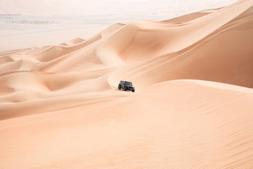 A single black car scaling giant sand dunes in the Empty Quarter desert. Abu Dhabi, UAE.