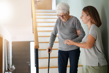 Homecare helping elderly woman going down the stairs - obrazy, fototapety, plakaty