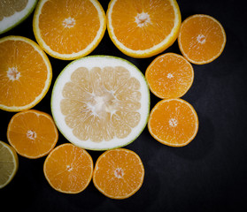 Citrus fruits (orange, lemon, grapefruit, mandarin, lime) on the dark background. Fruit food background. Sliced fresh citrus fruit assortment
