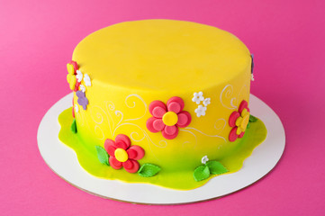 Colorful children's birthday cake made of yellow mastic decorated with pink flowers, leaves, pattern on a pink background. Close-up. Cutout. Picture for a menu or a confectionery catalog.