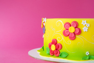 Colorful children's birthday cake made of yellow mastic decorated with pink flowers, leaves, pattern on a pink background. Close-up. Cutout. Picture for a menu or a confectionery catalog.