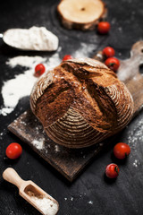 freshly baked bread, flour and tomatoes on a wooden board on a table