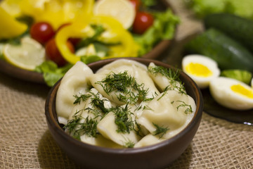 Obraz na płótnie Canvas Closeup view of traditional russian food - pelmeni, ravioli or meat dumplings. Served with eggs, tomatoes, salad, marinated mushrooms, sauerkraut, cucumbers, green onion and garlic. Copy space