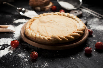 preparation for pizza, flour and tomatoes on a round wooden board on a black wooden table