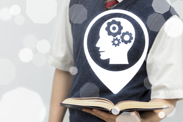 Teenager (young student, scientist, schoolboy) holds book with head gears location icon on a virtual screen. Brainstorm Knowledge System Educational concept.
