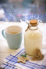 New Year's still-life with a bottle of milk, blue cup with coffee, biscuits, tablecloth in a box on a white wooden table, bright background on a sunny day