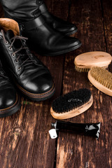 Fototapeta na wymiar Black boots on wooden background with polishing equipment, brush and polish cream.