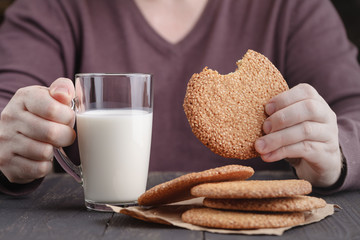Hands holding cup of coffee and cookies on black background