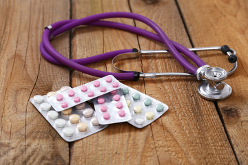 Medical stethoscope and tablets isolated on wooden background
