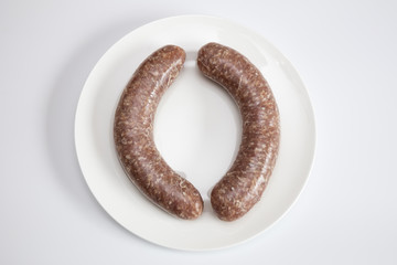 Zwei frische rohe Bratwürste auf einem weißen Teller