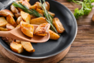Pieces of delicious baked potato with rosemary on spoon over pan, closeup