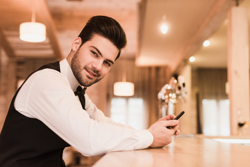 Waiter sitting at bar counter with smartphone