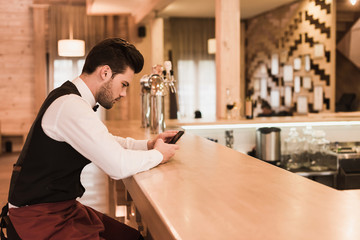 Waiter sitting at bar counter with smartphone