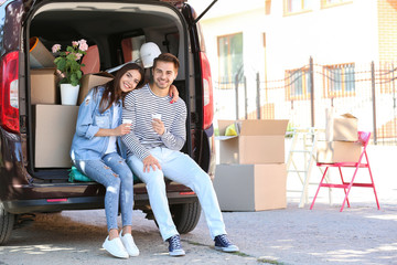 Young couple having break while putting their belongings in car trunk outdoors