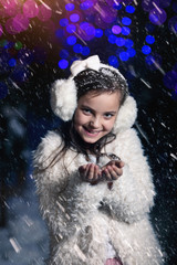Fototapeta premium Young girl blows snowflakes in winter evening