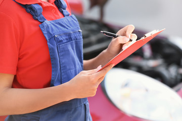 Obraz premium Young female mechanic with clipboard near car outdoors