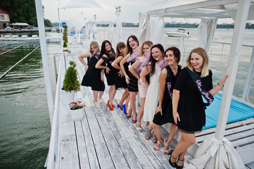 Group of 8 girls wear on black and 2 brides at hen party having fun at pier on beach side.