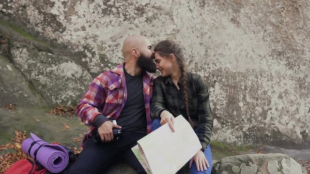 Young traveler photographers with a camera, tourist card and backpack, have fun sitting on the top of the mountain and have a rest. Loving young people