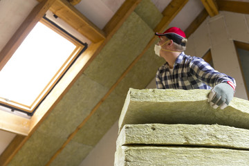 Man installing thermal roof insulation layer  - using mineral wool panels. Attic renovation and...