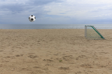 Obraz premium Soccer ball flying through the air above on sand beach field and entering the goal