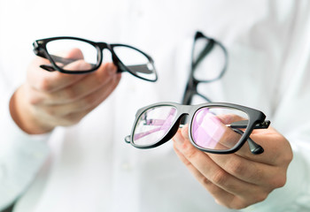 Optician comparing lenses or showing customer different options in spectacles. Eye doctor showing new glasses.