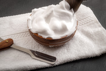 Male cosmetic products and supplies used by men to shave concept with a straight razor, towel, shaving brush and foam on dark grey background