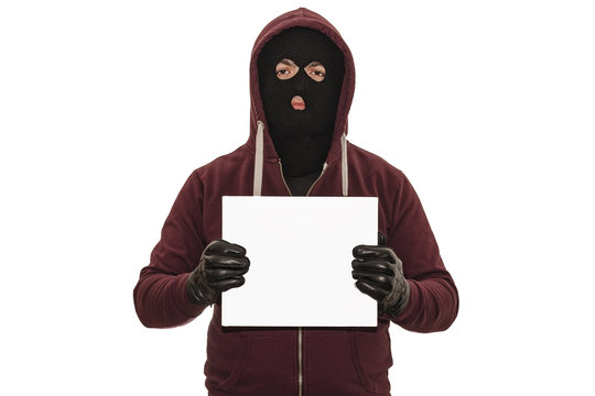 Police lineup or mugshot concept with a burglar or thief wearing a ski mask or balaclava and holding a blank white cardboard with copy space isolated on white background with clipping path