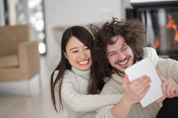 multiethnic couple using tablet computer in front of fireplace
