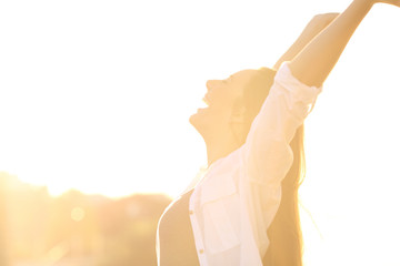 Excited woman raising arms at sunset