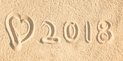 Close up on 2018 written in the sand of a beach wih a heart