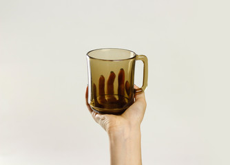 Female hand holding black empty glass mug. Isolated on gray background. Closeup