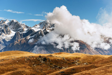 Autumn landscape and snow mountains in beautiful cumulus clouds. Main Caucasian Ridge. Type Mount Ushba Mheyer, Georgia