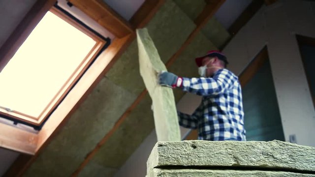 Man installing thermal roof insulation layer  - using mineral wool panels. Attic renovation and insulation concept