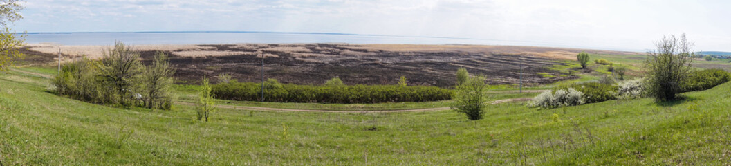 Panorama of the Volga River from the shore in the summer. Steppe banks of the Volga in Russia, burnt steppe grass, bush, road and the sight of a beautiful wide river to the horizon.