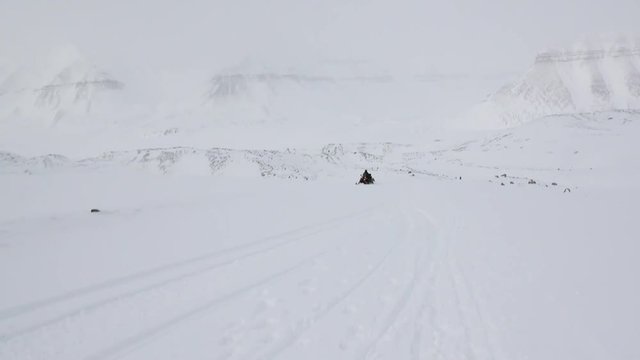 People expedition on snowmobile in North Pole Spitsbergen Svalbard Arctic. Way from airport Longyear to Pyramiden on background of glacier.