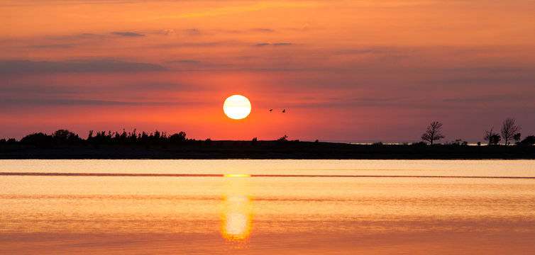 solneg&aring;ng vid vatten solen speglas i det lugna havet siluett av land vid horisonten