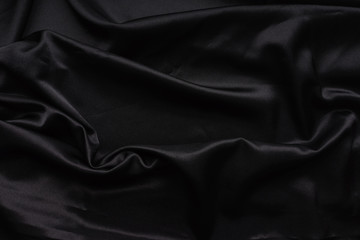 Dark black silky, satin  fabric, wave, draperies. Beautiful textile backdrop. Close-up. Top view 