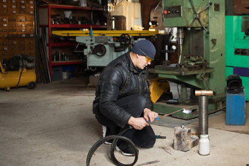 Work man is a welder in mask, metal product at home garage, with flame burning gas welding