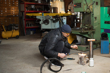 Fototapeta premium Work man is a welder in mask, metal product at home garage, with flame burning gas welding