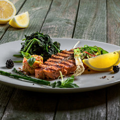 Plate with delicious grilled salmon fish steak and salad on a wooden table. Healthy gourmet food made of fish and vegetables.