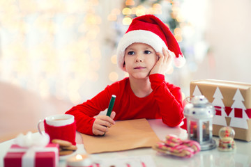 Boy writing letter to Santa Claus in red hat near the Christmas tree