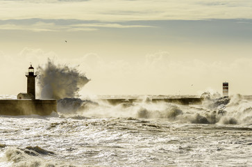 Landscape seascape lighthouse battered by huge waves on Atlantic Ocean with blue green skies and puffy clouds.