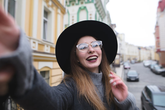 Stylish girl with braces takes selfie krasvoho against the background of the urban landscape. The girl tourist on background makes selfie beautiful streets of the old town.