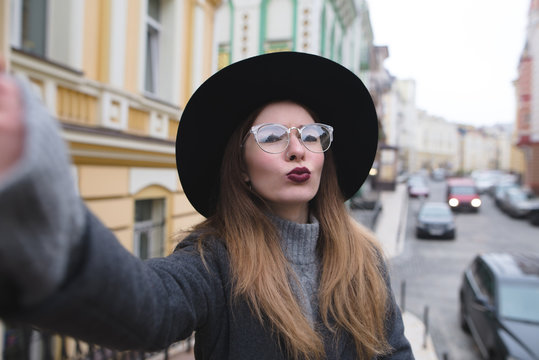 Stylish girl takes selfie street while walking around the beautiful city. Tourist hipster posing for the camera of your phone and make selfie.